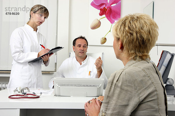 Arztpraxis  Arzt im Gespräch mit einer Patientin  bespricht mit ihr und einer Praxishilfe die anstehenden Untersuchungen