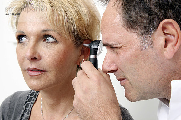 Arztpraxis  Arzt untersucht mit Hilfe einer beleuchteten Speziallupe den Gehörgang einer Patientin