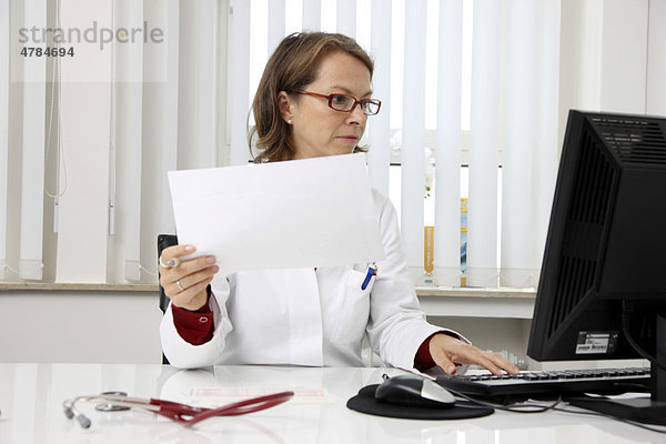 Arztpraxis  Ärztin schaut Patientenunterlagen an ihrem Schreibtisch durch
