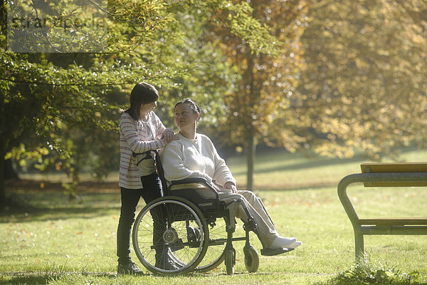 Frau im Rollstuhl mit ihrer Tochter im Park