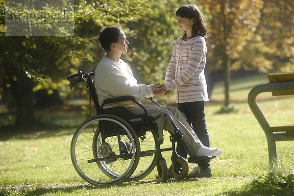Frau im Rollstuhl Hand in Hand mit ihrer Tochter im Park