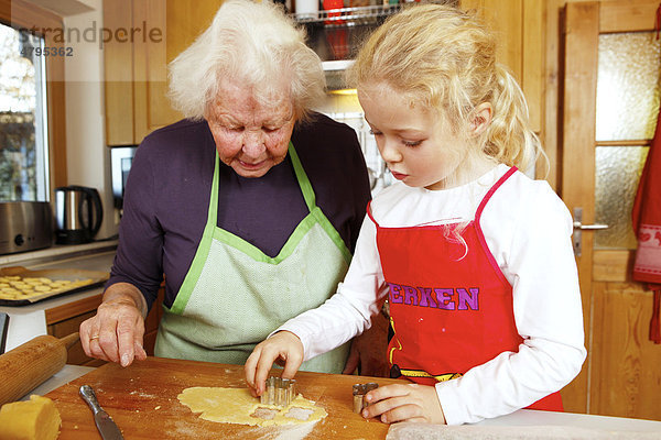 Weihnachtsbäckerei  Oma und Enkelin backen Weihnachtsplätzchen  Mädchen sticht mit Ausstechform den Teig aus
