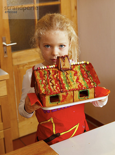 Weihnachtsbäckerei  Mädchen mit verziertem Lebkuchenhaus