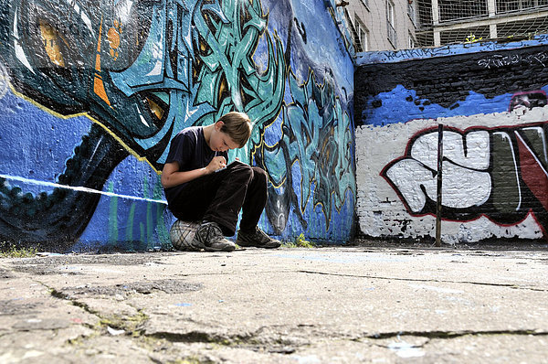 Zehnjähriger Junge spielt mit seinem Nintendo vor einer Graffitiwand  Bolzplatz  Deutschland  Europa