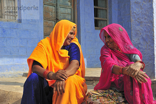 Zwei lächelnde Inderinnen in leuchtend bunten Saris unterhalten sich vor ihrem Haus  Rajasthan  Indien  Asien