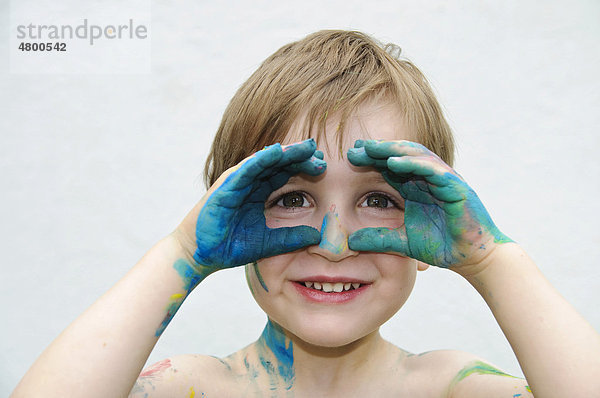 Kleiner Junge  3 Jahre  schaut durch seine mit Fingerfarbe bemalten Hände
