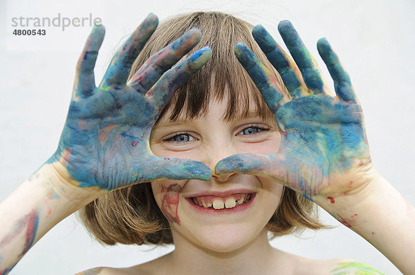 Mädchen  8 Jahre  schaut durch ihre mit Fingerfarbe bemalten Hände