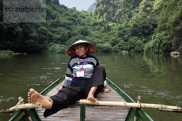 Frau rudert mit Füßen  Umgebung von Ninh Binh  unterwegs am Fluss zu den Höhlen von Trung Anh  trockene Halong Bucht  Vietnam  Südostasien
