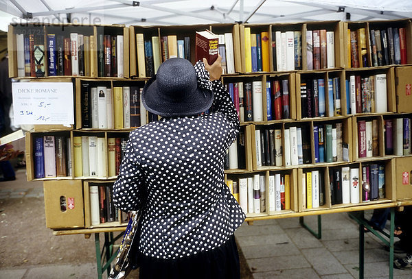 Ältere Frau nimmt dicken Roman aus einem Verkaufsregal  Open-Air-Büchermarkt auf der Königsalle  Kö  Düsseldorf  Nordrhein-Westfalen  Deutschland  Europa
