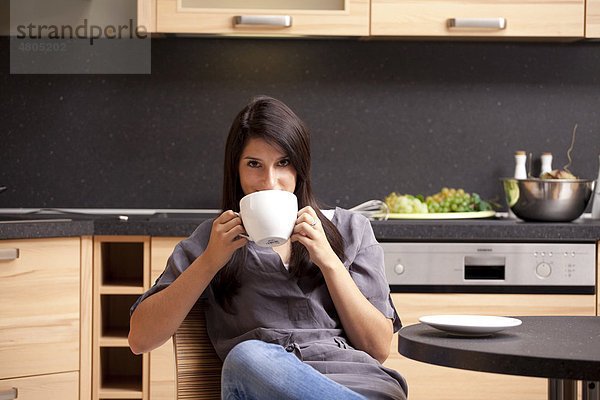 Junge Frau sitzt in der Küche und trinkt Kaffee