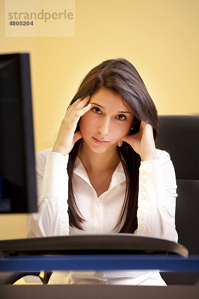 Junge Frau sitzt genervt im Büro am Computer
