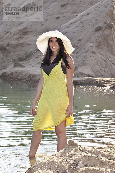 Junge Frau mit Strohhut am Strand eines Baggersees