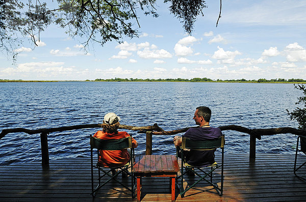 Touristen sitzen auf einer Terrasse einer Lodge über der Guma Lagune  Guma Lagoon  Okavango-Delta  Botsuana  Afrika