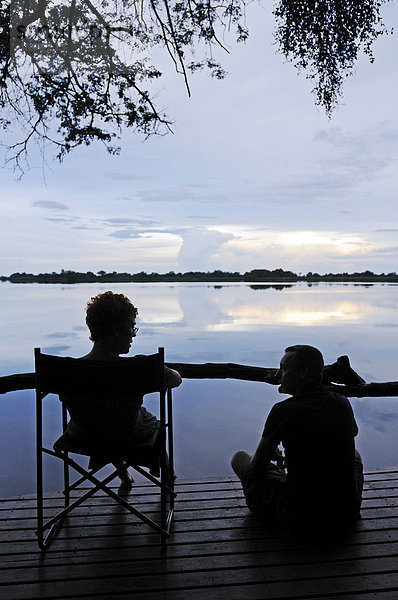 Touristen sitzen in Abendstimmung auf einer Terrasse über der Guma Lagune  Guma Lagoon  Okavango-Delta  Botsuana  Afrika