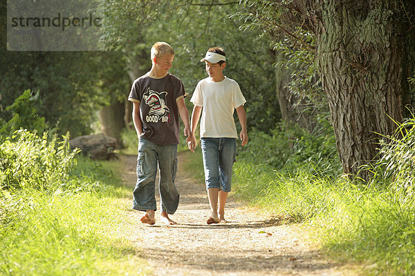Zwei Jungen gehen barfuss einen Waldweg entlang