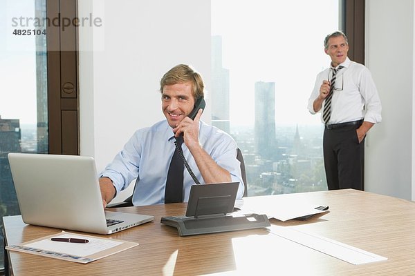 Geschäftsmann am Telefon mit Mann im Hintergrund