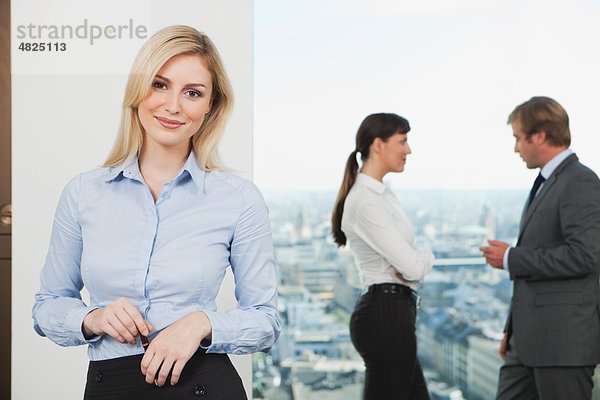Geschäftsfrau lächelt mit Geschäftsleuten  die im Hintergrund reden