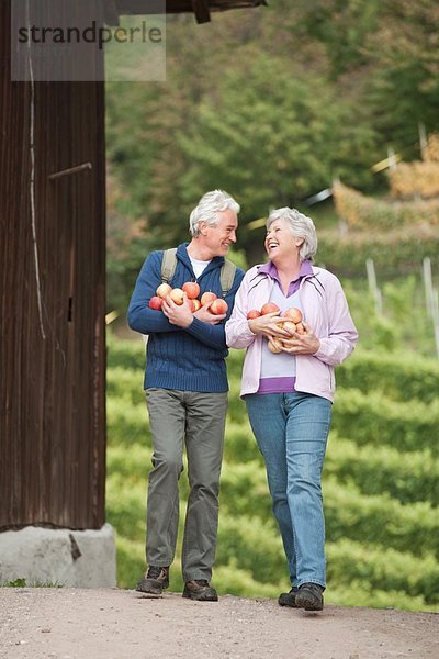 Italien  Südtirol  Äpfel tragendes reifes Paar  lächelnd