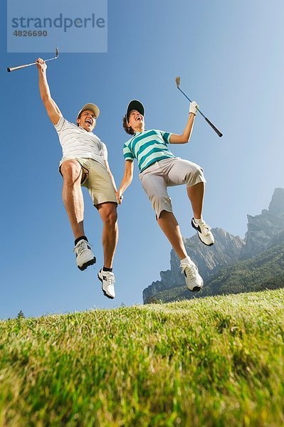 Italien  Kastelruth  Mittleres erwachsenes Paar beim gemeinsamen Springen auf dem Golfplatz