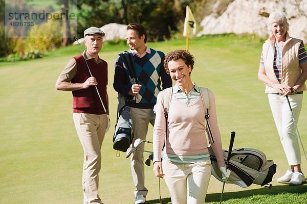 Italien  Kastelruth  Mittlere erwachsene Frau lächelnd mit Golfern im Hintergrund auf dem Golfplatz