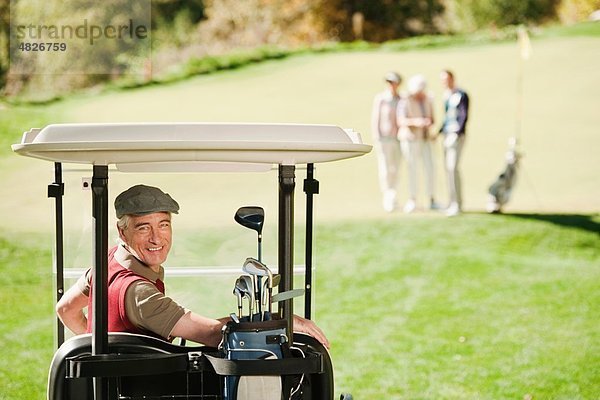 Italien  Kastelruth  Reifer Mann im Golfwagen mit Golfern auf dem Golfplatz