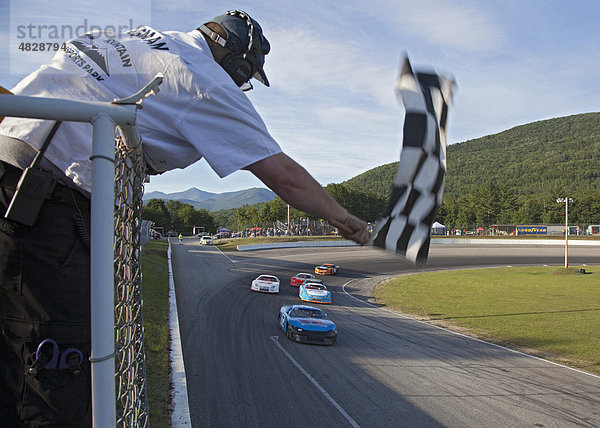 Ein Streckenposten schwenkt die Zielflagge während eines Stockcar-Rennens  White Mountain Motorsports Park  Woodstock  New Hampshire  USA