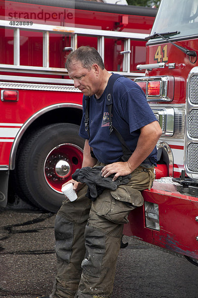 Ein erschöpfter Feuerwehrmann macht eine Pause von den Löscharbeiten an einem Hausbrand bei heißem Sommerwetter  Detroit  Michigan  USA