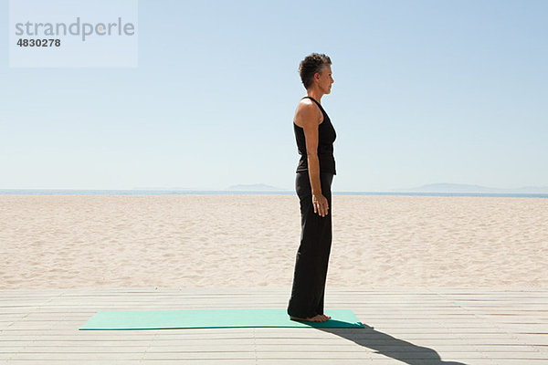 Seniorin beim Yoga am Strand