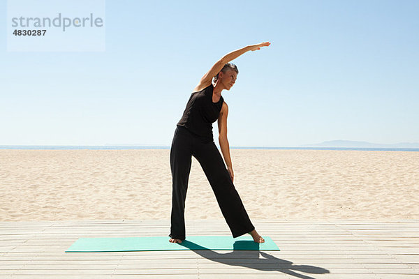 Seniorin beim Yoga am Strand