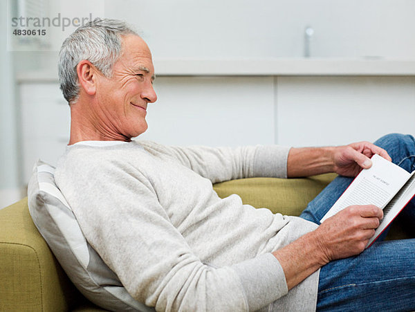 Älterer Mann auf Sofa sitzend Lesebuch