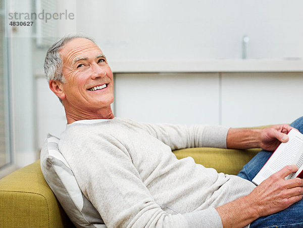 Älterer Mann auf Sofa sitzend Lesebuch
