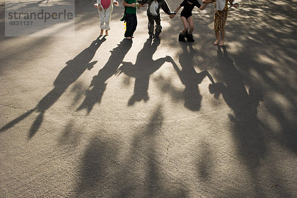 Fünf Kinder im Kostüm  die sich an den Händen halten und Schatten werfen.