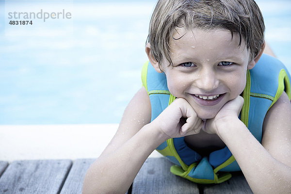 Junge in Schwimmweste an der Seite des Pools lehnend  Portrait