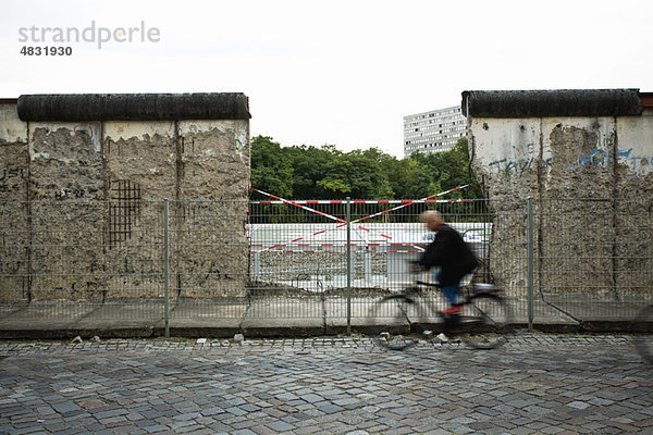 Deutschland  Berlin  Person  die an einem abgebauten Teil der Berliner Mauer vorbeifährt.
