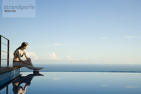 Frau sitzt am Rande des Infinity Pools und schaut auf die Aussicht.