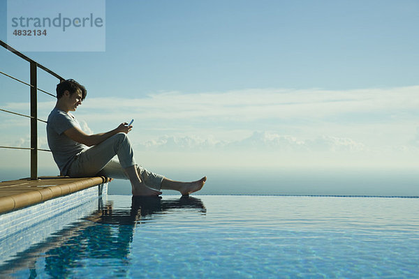 Mann am Rande des Infinity Pools  SMS mit Handy