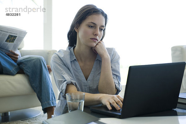 Junge Frau sitzt am Couchtisch und benutzt einen Laptop