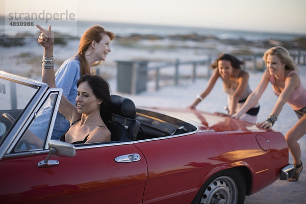 Gruppe von Mädchen  die ein kaputtes Auto schieben.