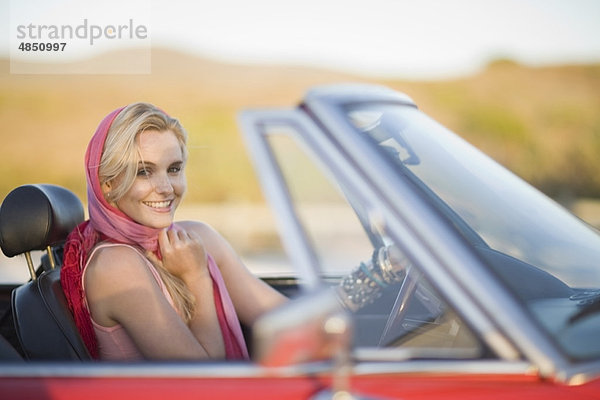 Blonde Frau mit rotem Schal im Cabriolet