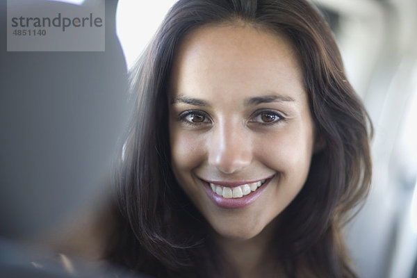 Junge Frau mit dunklem Haar im Auto lächelnd