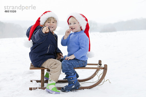 Zwei Jungen auf einem Schlitten mit Weihnachtsmützen