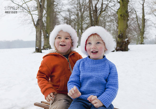 Zwei Jungen mit flauschigen Hüten im Schnee