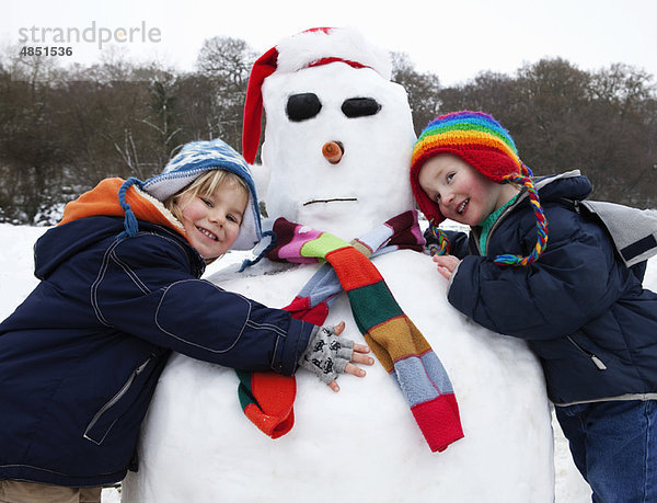 Zwei Jungen  die einen Schneemann umarmen.