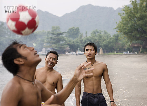 Kerle  die am Strand Fußball spielen