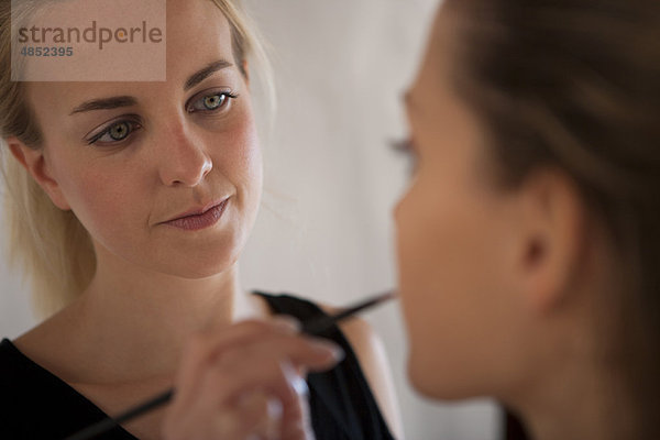 Make-up Artist beim Auftragen von Lippenstift auf das Modell mit Lippenpinsel und Mund