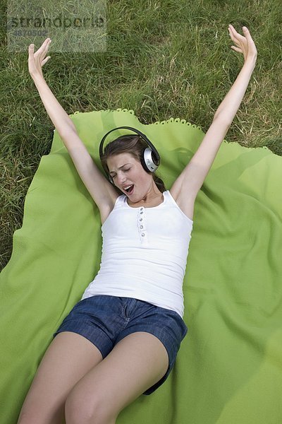 Fröhliche junge Frau hört Musik auf einer Wiese