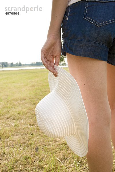 Junge Frau mit Shorts und Hut auf einer Wiese