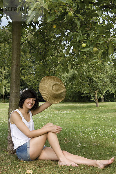 Fröhliche junge Frau sitzt an einem Apfelbaum
