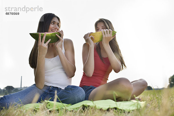 Zwei junge Frauen essen Melonen im Freien