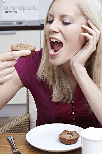 Blonde junge Frau isst Gebäck